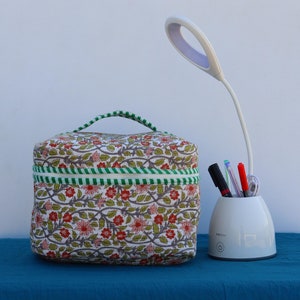 May include: A white desk lamp with a flexible arm and a white base with a built-in pencil holder. The lamp is next to a floral patterned fabric makeup bag.