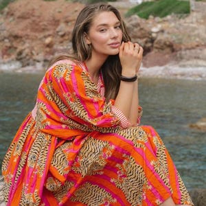 Puede incluir: Vestido vibrante con estampado de rayas de tigre y rayas verticales en naranja y rosa. El vestido tiene mangas largas y una falda fluida. El texto "BABITA TEX" es visible en la parte inferior del vestido.