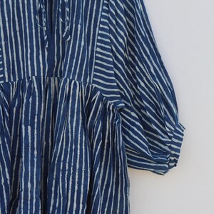May include: A navy blue and white striped dress featuring a round neckline with a tie closure, gathered fabric at the bodice, and three-quarter length puff sleeves. The garment displays a vertical stripe pattern throughout with a contrasting horizontal stripe detail on the sleeves.