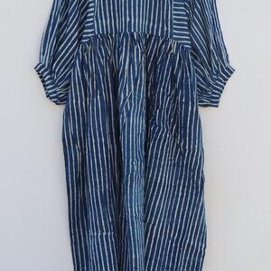 May include: A midi-length dress in deep indigo blue with a white vertical stripe pattern. The garment features three-quarter length sleeves with gathered cuffs, a round neckline, and a gathered waistline that creates a full, flowing skirt silhouette.