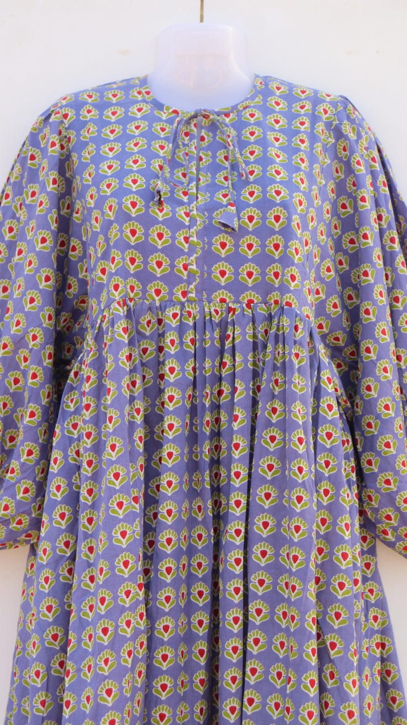 Puede incluir: Un vestido largo de manga larga de color morado con estampado floral rojo y verde. El vestido tiene una cintura fruncida y un lazo en el escote.