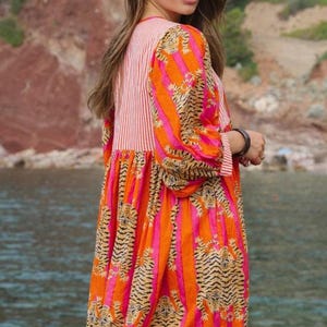Puede incluir: Vestido estampado con rayas de tigre y rayas en naranja y rosa. El vestido tiene mangas largas y un corpi&ntilde;o a rayas. El texto "BATTATEX" es visible en la parte inferior de la imagen. El vestido lo lleva una persona.