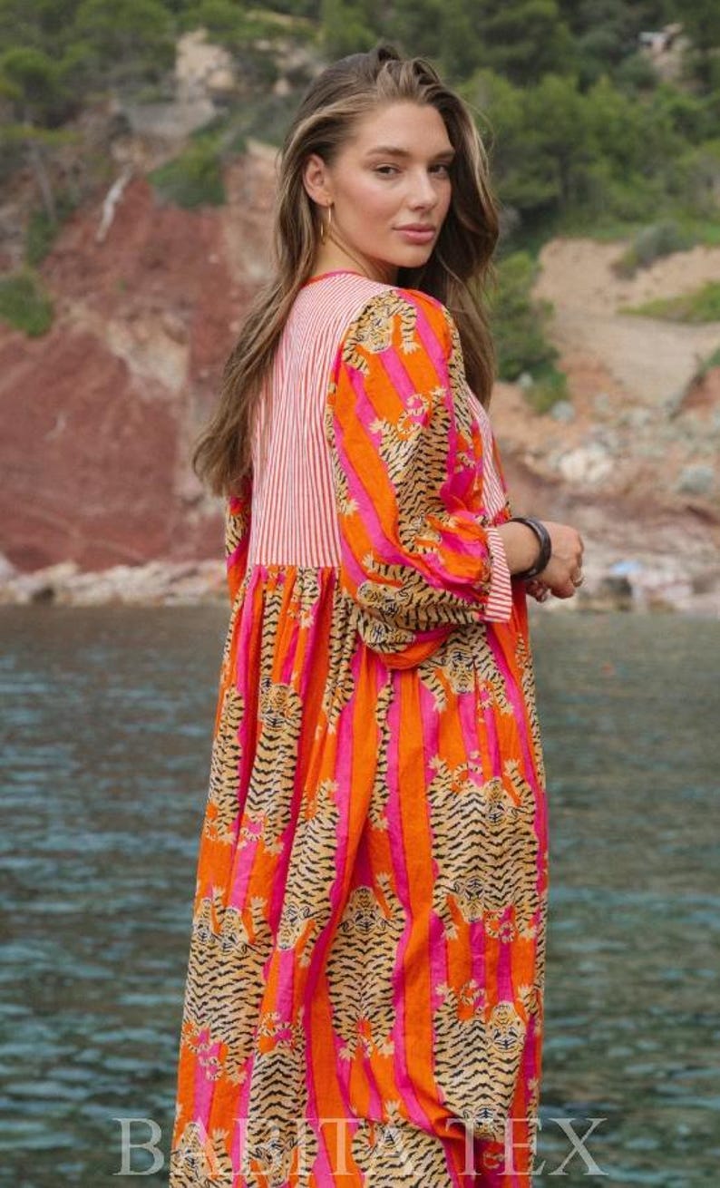 Puede incluir: Vestido estampado con rayas de tigre y rayas en naranja y rosa. El vestido tiene mangas largas y un corpi&ntilde;o a rayas. El texto "BATTATEX" es visible en la parte inferior de la imagen. El vestido lo lleva una persona.