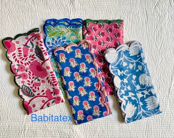 Pode incluir: Cinco guardanapos de algodão com bordas festoneadas e padrões florais em tons de rosa, azul e verde. Os guardanapos estão dobrados e dispostos sobre uma superfície branca. O texto "Babitatex" é visível no canto inferior esquerdo da imagem.