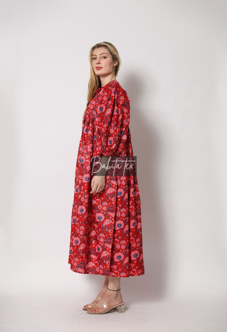 Puede incluir: Un vestido maxi rojo con estampado floral. El vestido tiene un escote en V, mangas largas y una falda fruncida. El vestido est&aacute; hecho de algod&oacute;n y es perfecto para un d&iacute;a de verano.