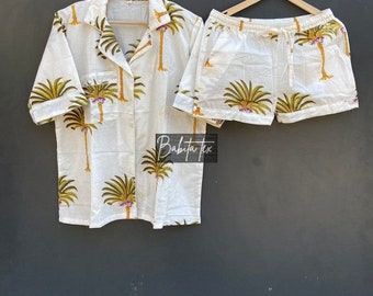May include: A white pajama set with a short-sleeved button-up shirt and matching shorts. Both pieces feature a palm tree print in shades of green, yellow, and brown.