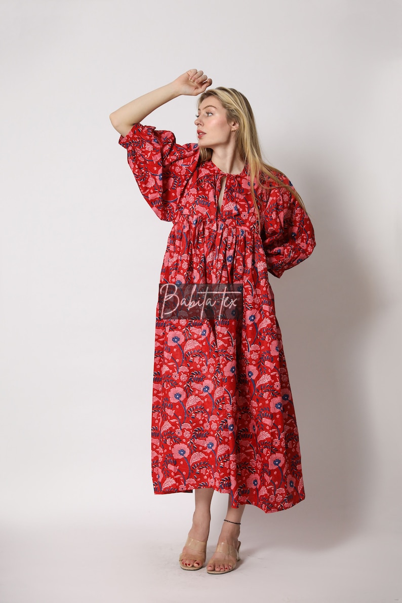 Puede incluir: Un vestido maxi rojo con estampado floral y un lazo en el cuello. El vestido tiene una falda fruncida y mangas abullonadas.