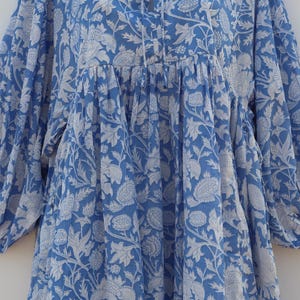 May include: A blue cotton dress with a white floral print. The dress has a gathered waist and a tie at the neckline.