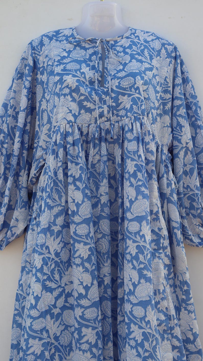 May include: A blue cotton dress with a white floral print. The dress has a gathered waist and a tie at the neckline.