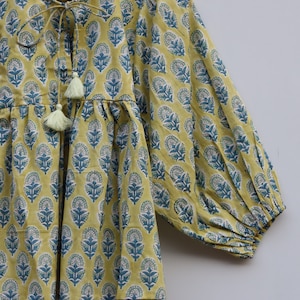 May include: A yellow cotton top with a blue floral print and a tie at the neckline. The top has a gathered waist and 3/4 sleeves.