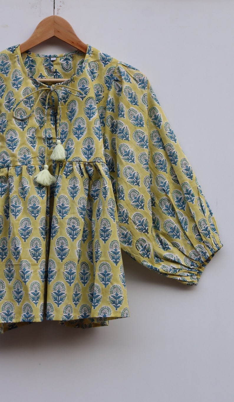 May include: A yellow cotton top with a blue floral print and a tie at the neckline. The top has a gathered waist and 3/4 sleeves.
