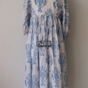 May include: A white dress with a blue floral print. The dress has a gathered waist and 3/4 sleeves. The dress is on a mannequin.