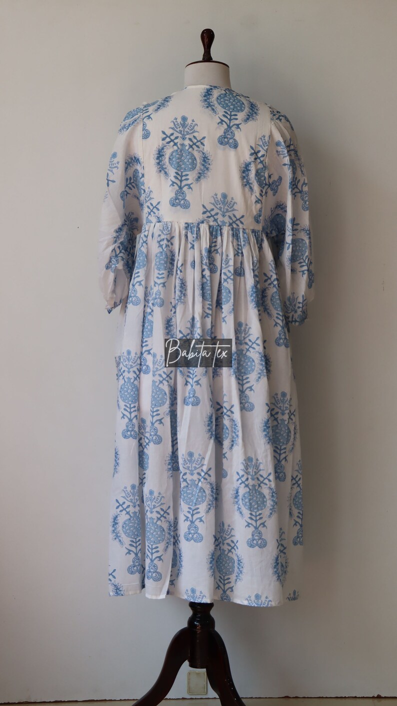 May include: A white dress with a blue floral print. The dress has a gathered waist and 3/4 sleeves. The dress is on a mannequin.