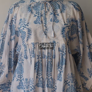 May include: White cotton dress with a blue floral print and a tie at the neck. The dress has a gathered waist and 3/4 sleeves. The dress is made by Babita Tex.