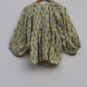 May include: A yellow cotton top with a blue floral print and long, puffed sleeves. The top has a gathered waist and a round neckline.