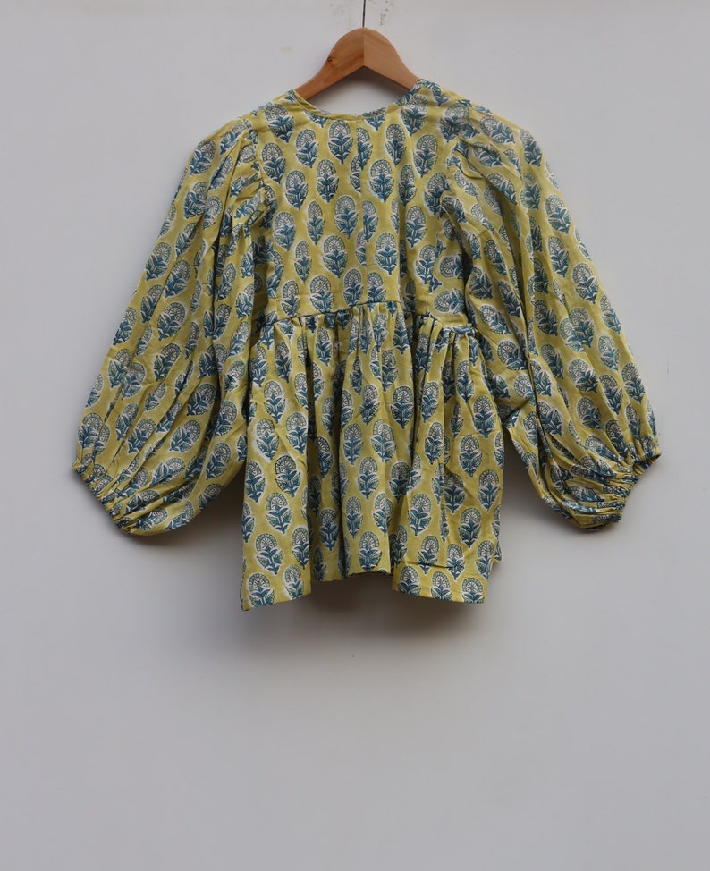 May include: A yellow cotton top with a blue floral print and long, puffed sleeves. The top has a gathered waist and a round neckline.