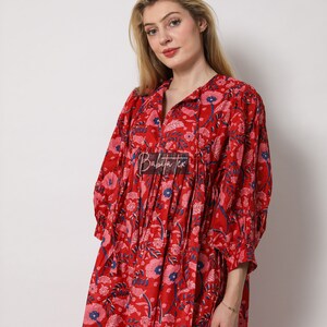 Puede incluir: Un vestido rojo de estampado floral con cuello en V y mangas 3/4. El vestido tiene una cintura fruncida y una falda fluida. El vestido est&aacute; hecho de algod&oacute;n y es perfecto para un d&iacute;a de verano.
