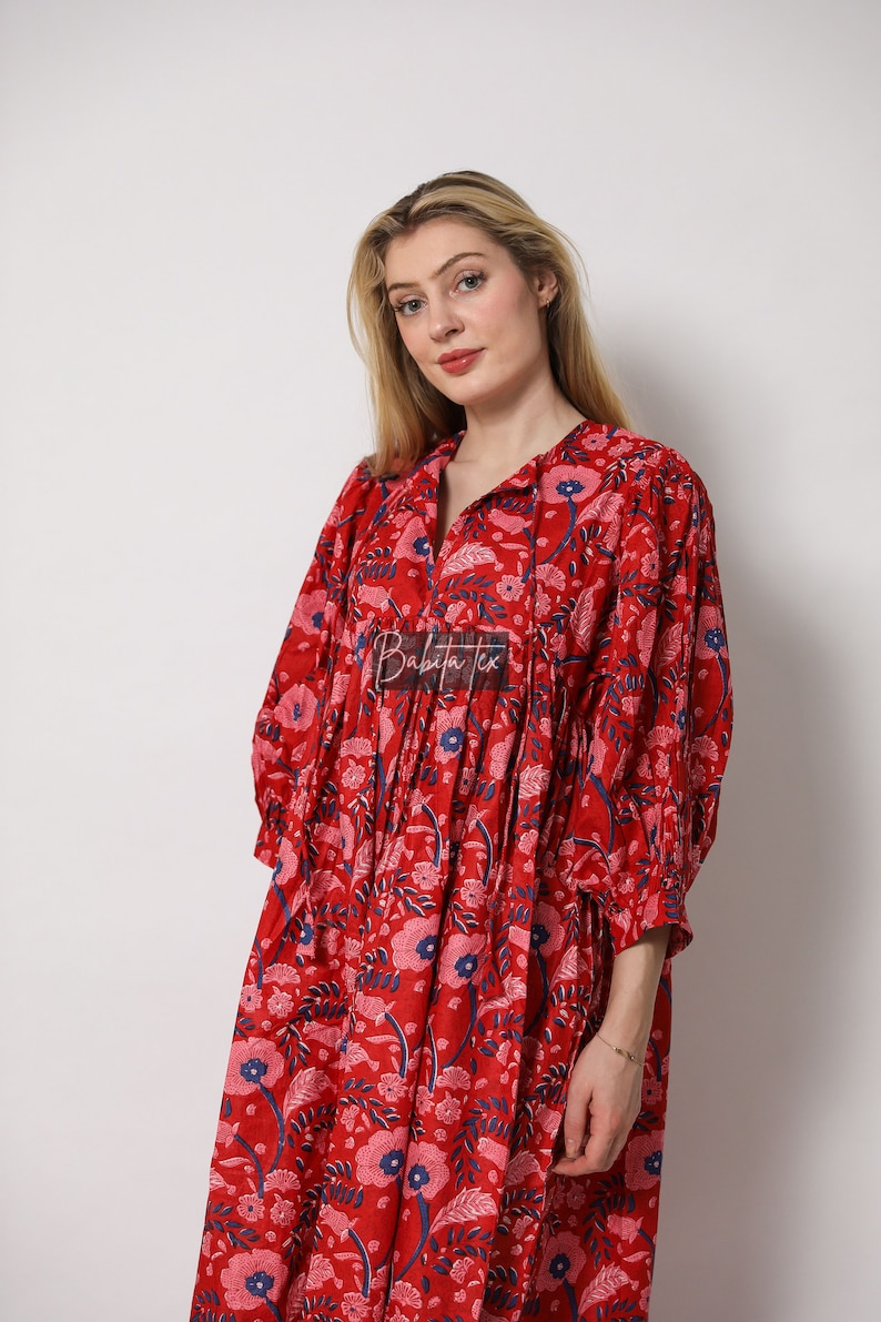 Puede incluir: Un vestido rojo de estampado floral con cuello en V y mangas 3/4. El vestido tiene una cintura fruncida y una falda fluida. El vestido est&aacute; hecho de algod&oacute;n y es perfecto para un d&iacute;a de verano.