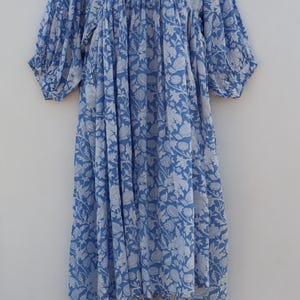 May include: A light blue cotton dress with a white floral print. The dress has a round neckline, 3/4 sleeves, and a gathered waist.