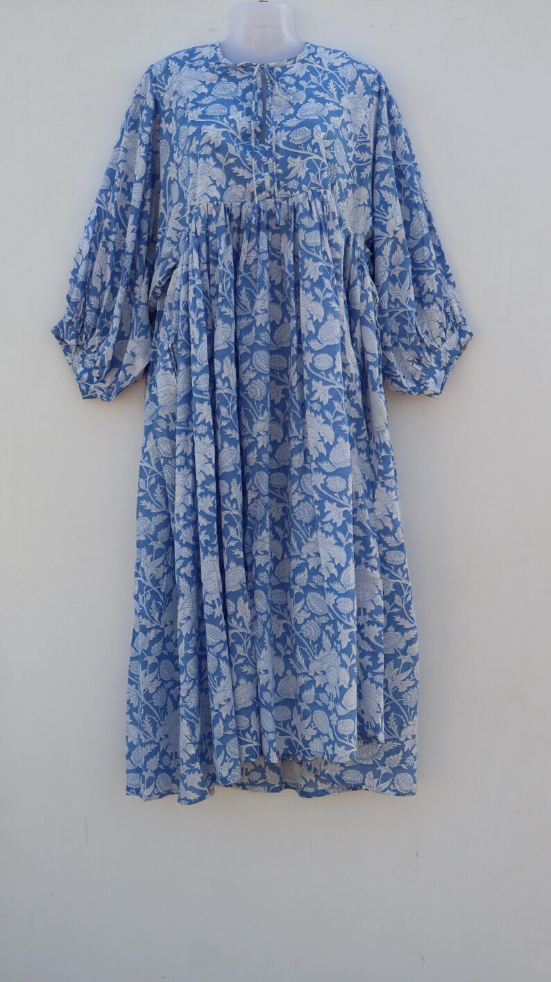May include: A light blue cotton dress with a white floral print. The dress has a round neckline, 3/4 sleeves, and a gathered waist.