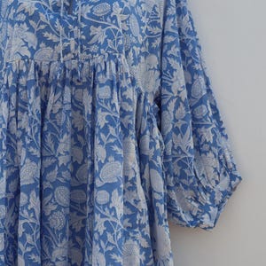 May include: A blue and white floral print dress with a gathered bodice and 3/4 sleeves. The dress has a tie at the neckline.