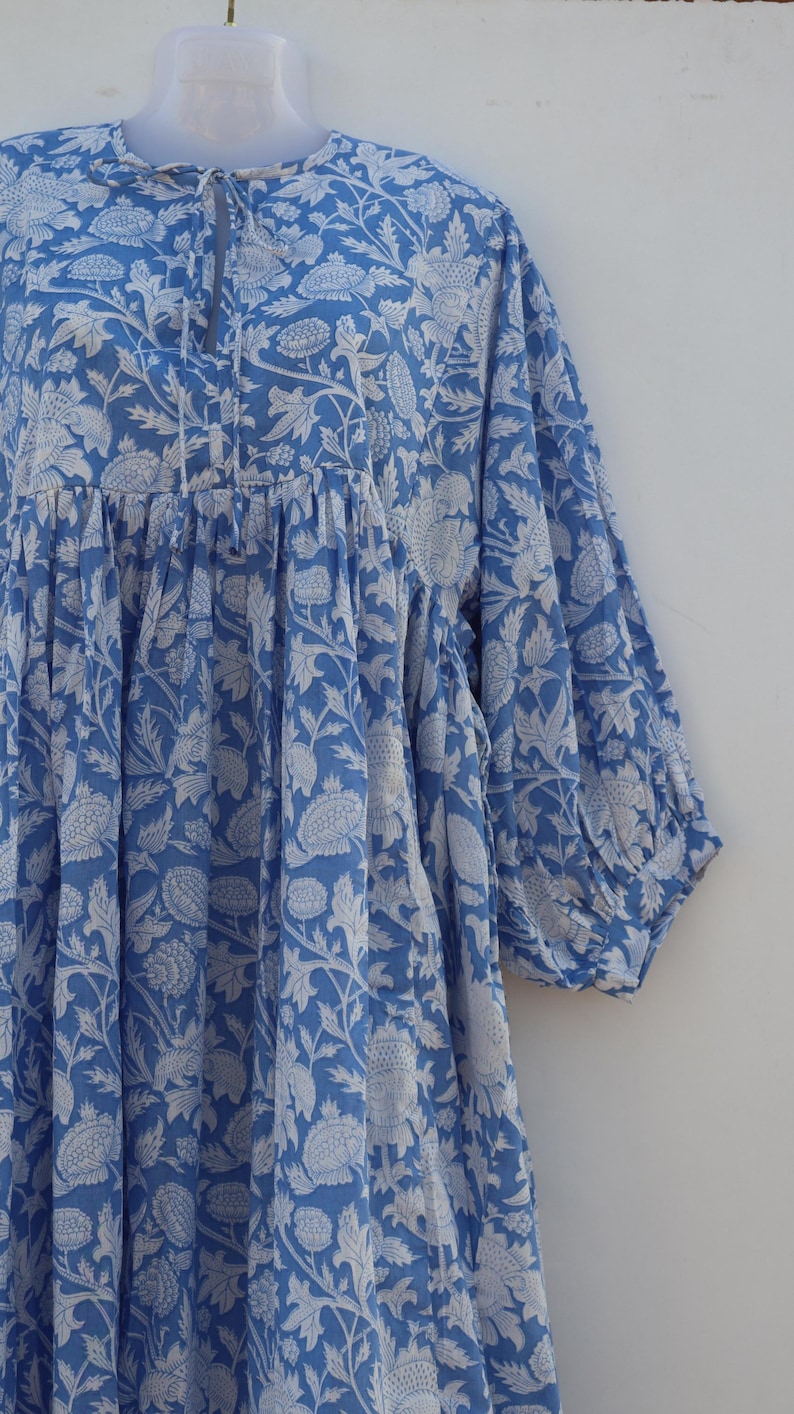 May include: A blue and white floral print dress with a gathered bodice and 3/4 sleeves. The dress has a tie at the neckline.