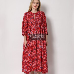 Puede incluir: Un vestido maxi rojo con estampado floral y un lazo en el cuello. El vestido tiene una falda fruncida y mangas 3/4.