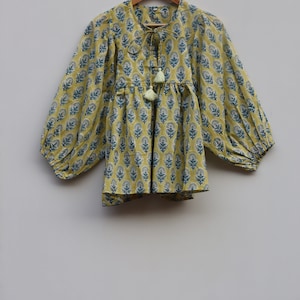 May include: A yellow cotton top with a blue floral print and a tie at the neck. The top has long sleeves with a gathered cuff and a gathered waist.