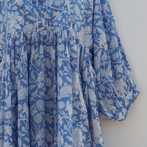 May include: A blue cotton dress with a white floral print. The dress has a gathered waist and a tie at the neckline.