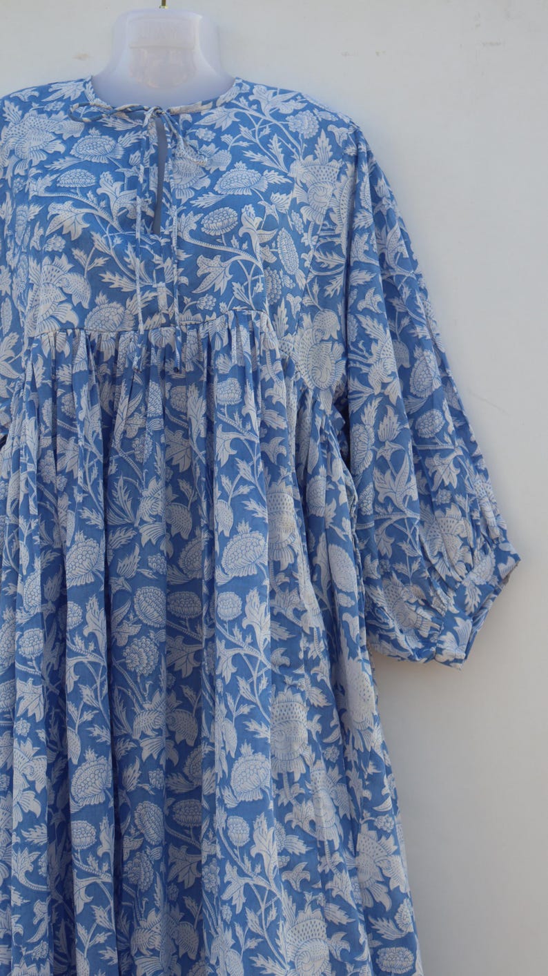 May include: A blue cotton dress with a white floral print. The dress has a gathered waist and a tie at the neckline.