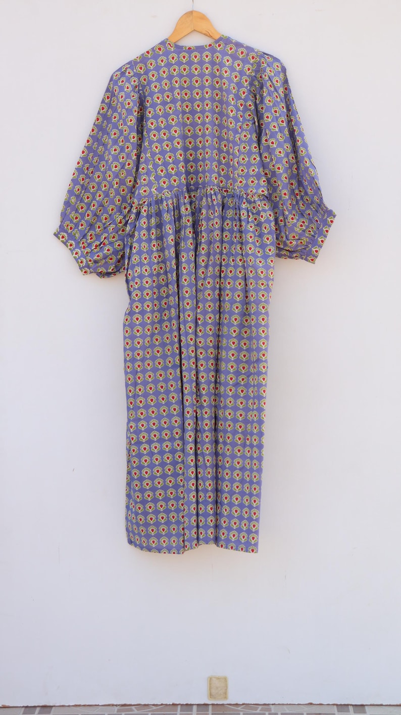 Puede incluir: Un vestido morado con estampado floral con flores rojas, amarillas y blancas. El vestido tiene una cintura fruncida y mangas abullonadas.