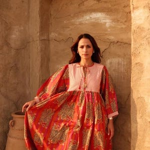 Puede incluir: Un vestido largo y fluido de color rojo con estampado de tigre y corpi&ntilde;o a rayas. El vestido tiene mangas largas y lo lleva una persona. El texto "BABITA TEX" es visible en la parte inferior de la imagen. Es una prenda vibrante.
