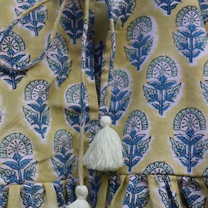 May include: A yellow cotton top with a blue and green floral print. The top has a tie at the neck and tassels at the bottom.