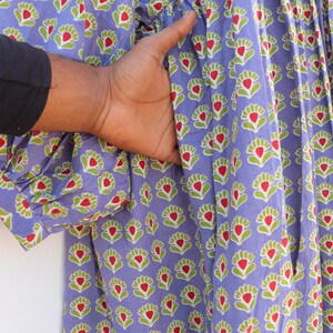 Puede incluir: Un vestido largo de algod&oacute;n azul con estampado floral con flores rojas y verdes. El vestido tiene una falda fruncida y un frente abotonado.