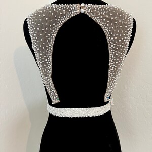 May include: A white beaded bodice with a low back and a beaded belt. The bodice is made of a sheer fabric with small white beads sewn on.