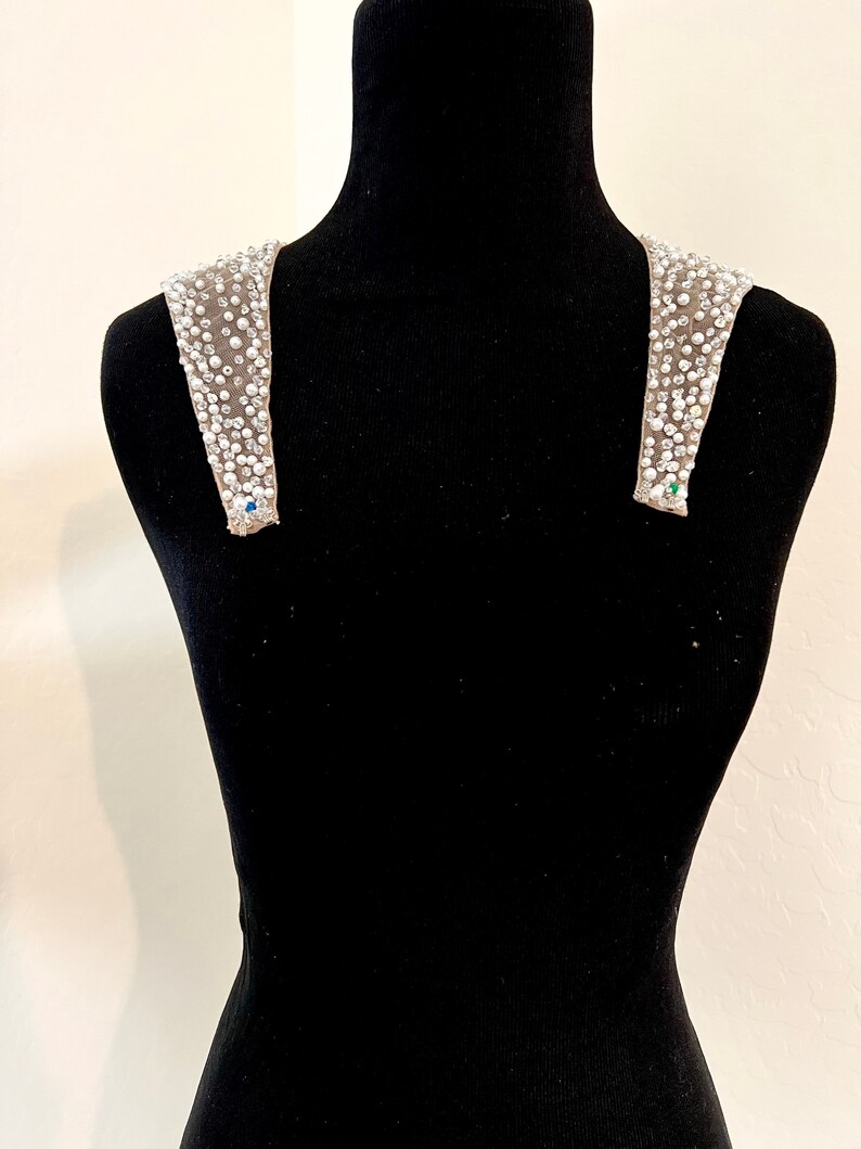 May include: A pair of beaded shoulder straps with a light brown fabric base. The straps are adorned with small, white beads and rhinestones.