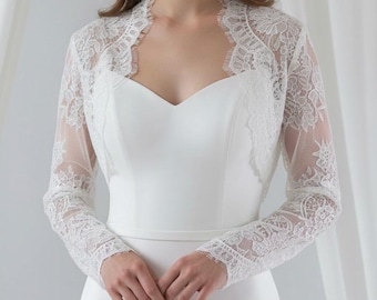May include: A white long-sleeved lace bolero jacket featuring intricate floral patterns and scalloped edges, worn over a matching white sweetheart neckline dress. The bolero has sheer sleeves and a fitted bodice that complements the smooth fabric of the dress.