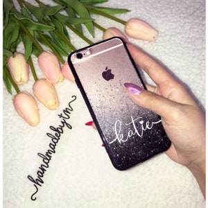 May include: A black and silver glitter phone case with the name "katie" written in white cursive. The case is handmade and has a gradient effect.