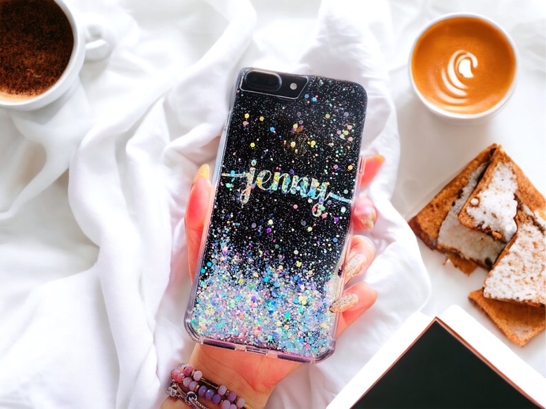 May include: A black glitter phone case with a holographic finish. The case has the name "Jenny" written in gold glitter on the back.