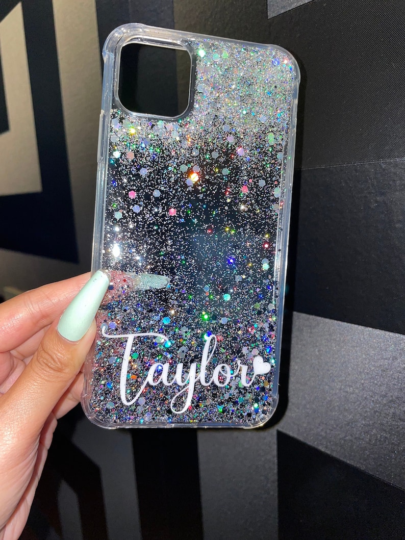 May include: A clear phone case with a silver glitter design and the name "Taylor" written in white with a small white heart.