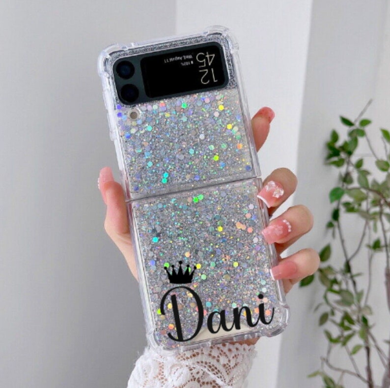 Pu&ograve; includere: Una custodia per telefono trasparente con un design a glitter argentati. La custodia ha una corona e il nome "Dani" stampato.