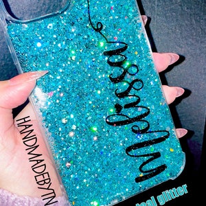 Pu&ograve; includere: Una custodia per telefono trasparente con uno sfondo di glitter verde acqua e la parola "miss you" scritta in corsivo nero. La custodia ha un bordo trasparente e le parole "HANDMADEBYTN" e "green teal glitter" sono scritte in basso.