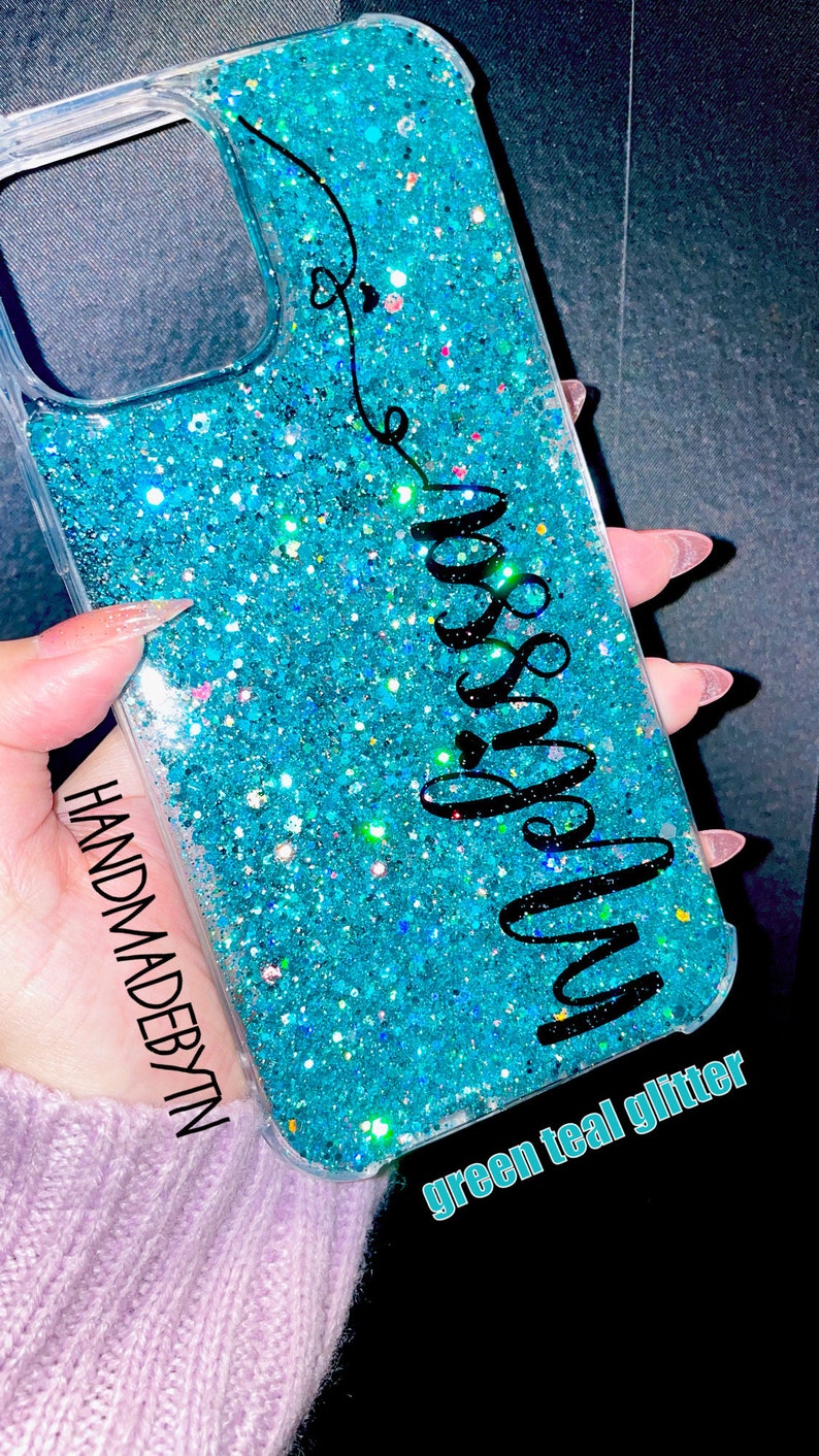 Pu&ograve; includere: Una custodia per telefono trasparente con uno sfondo di glitter verde acqua e la parola "miss you" scritta in corsivo nero. La custodia ha un bordo trasparente e le parole "HANDMADEBYTN" e "green teal glitter" sono scritte in basso.