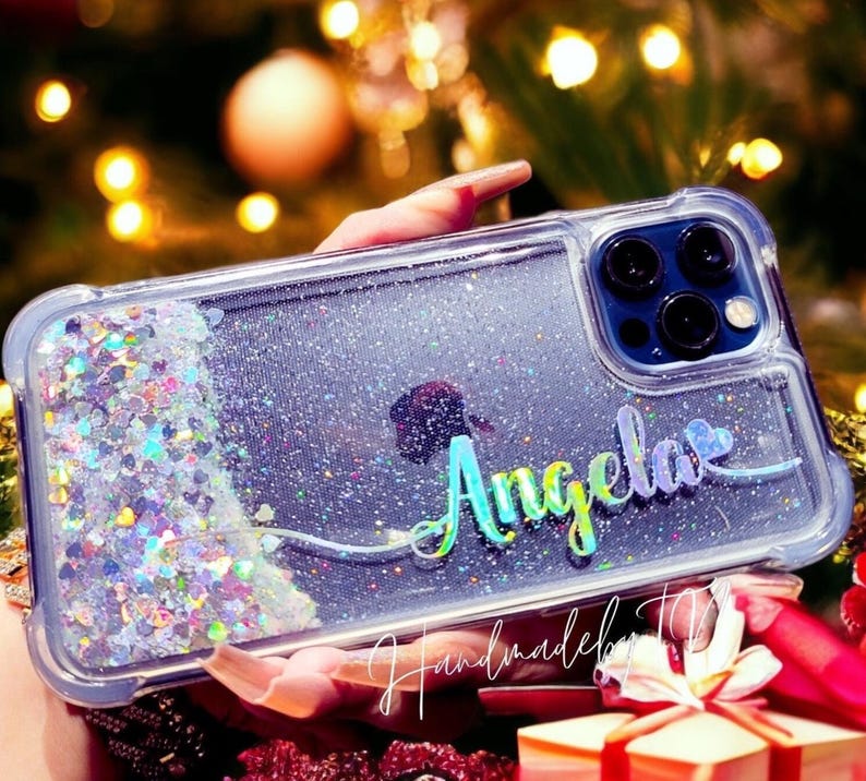 May include: A clear phone case with a glittery background and the name "Angela" written in rainbow colors. The case has a cutout for the phone's camera.