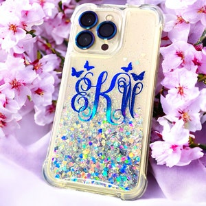May include: A clear phone case with a glittery background and blue butterflies. The case has a blue monogram "EK" in the center.