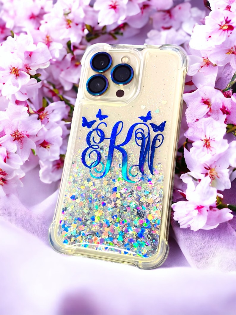 May include: A clear phone case with a glittery background and blue butterflies. The case has a blue monogram "EK" in the center.