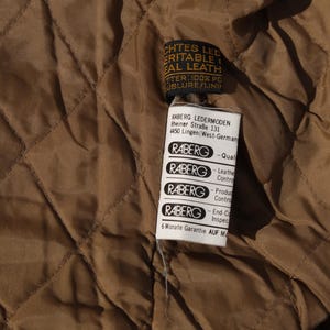 May include: Close-up of a brown quilted fabric with a tag attached. The tag has text that reads "ECHTES LEDER, ERITABLE REAL LEATHER". The tag also has the brand name "RABERG" and other text.