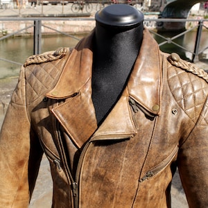 May include: Brown leather jacket with a distressed finish, featuring a quilted shoulder design and a classic asymmetrical zipper. The jacket has a notched lapel and multiple zippered pockets, showcasing a vintage aesthetic.