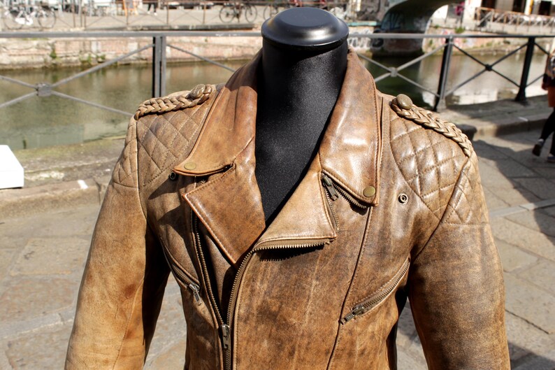 May include: Brown leather jacket with a distressed finish, featuring a quilted shoulder design and a classic asymmetrical zipper. The jacket has a notched lapel and multiple zippered pockets, showcasing a vintage aesthetic.