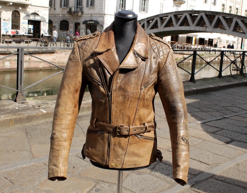 May include: A brown leather jacket with a belted waist and quilted shoulder details. The jacket has a zipper closure, multiple pockets, and a classic biker style. The jacket is displayed on a mannequin.